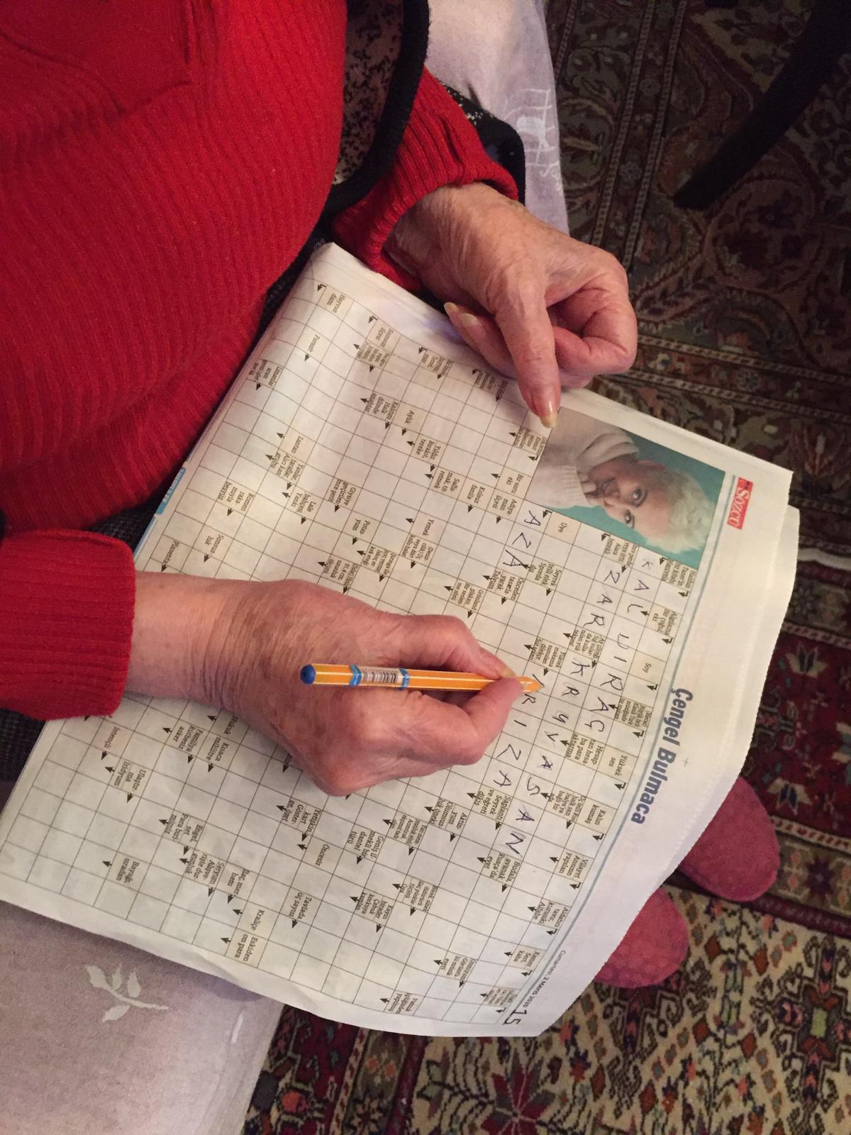Hands of a aged women, does a crossword puzzle on a newspaper.
